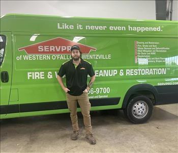 SERVPRO male employee with a black SERVPRO shirt and khaki pants on on standing in front of a green SERVPRO van