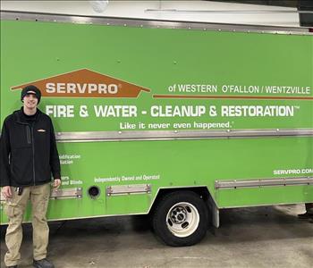 SERVPRO male employee with a black sweater and black knit hat on on standing in front of a green SERVPRO truck